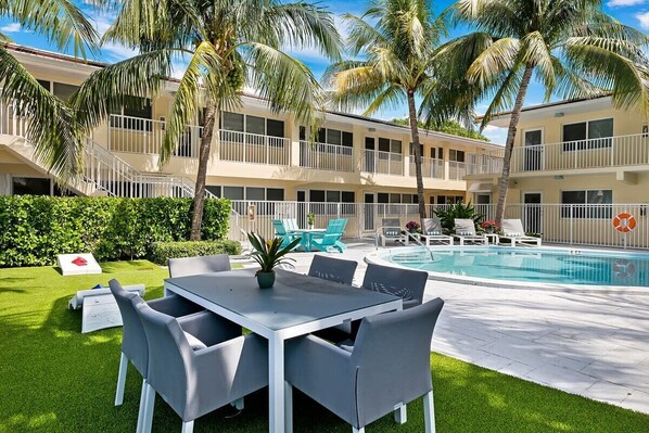 A hotel with a pool, outdoor seating, and palm trees.