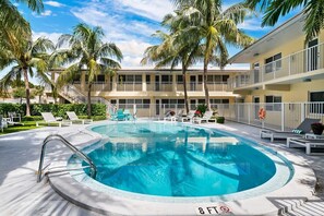 A swimming pool surrounded by palm trees and lounge chairs, with a building in the background.