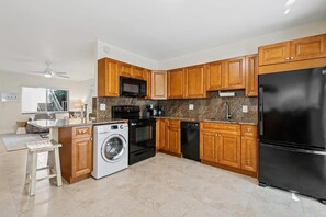 A modern kitchen with wooden cabinets, a black refrigerator, a microwave, a stove, and a washing machine.