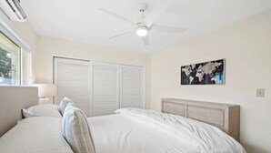 A bedroom with a bed, a ceiling fan, a window, and a world map on the wall. - Bermuda Isles Villas - King #23 (Lauderdale-by-the-Sea)