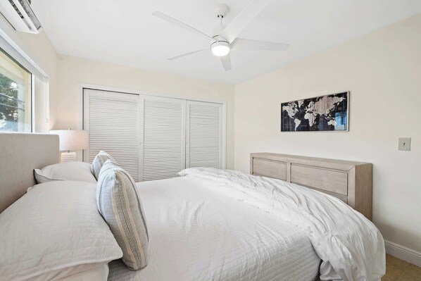 A bedroom with a bed, a ceiling fan, a window, and a world map on the wall. - Bermuda Isles Villas - King #23 (Lauderdale-by-the-Sea)