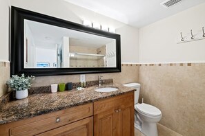 A bathroom with a granite countertop, a white sink, a mirror, and a toilet.