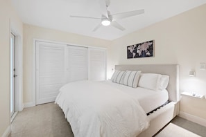 A bedroom with a bed, a ceiling fan, a wall-mounted light, and a door with a view of the outside.