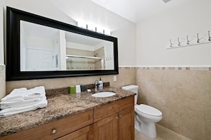 A bathroom with a granite countertop, a sink, a toilet, and a large mirror.