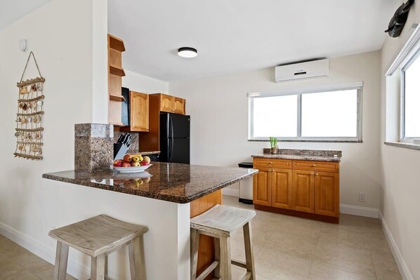 A kitchen with granite countertops, wooden cabinets, a black refrigerator, and a window providing natural light.