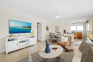 A modern living room with a flat-screen TV, a dining area, and a kitchen.