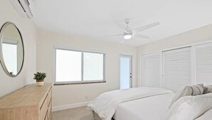 A bedroom with a bed, a ceiling fan, a window, a door, and a wooden dresser. - Bermuda Isles Villas - King #32 (Lauderdale-by-the-Sea)