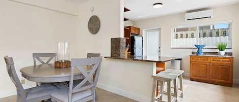 A modern kitchen with a central island, wooden cabinets, and a dining area with grey chairs.