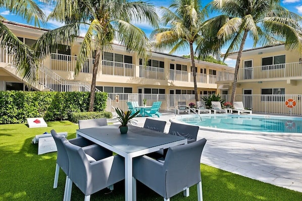 Un hotel con piscina, mobiliario exterior y palmeras.