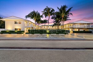 A hotel with a two-story structure, a covered parking area, and palm trees. - Bermuda Isles Villas - Queen #10 (Lauderdale-by-the-Sea)