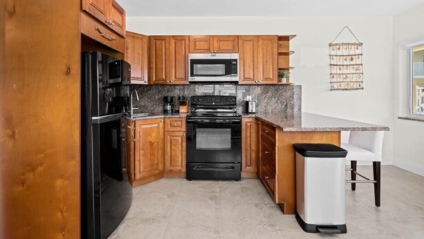 Una cocina con armarios de madera, una estufa negra, un microondas y un cesto de basura.