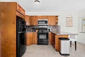Una cocina con armarios de madera, una estufa negra, un microondas y un cesto de basura.