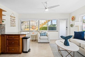 A modern kitchen with a white ceiling fan, a dining area with a white table and chairs, and a view of a balcony with a railing. - Bermuda Isles Villas - Queen #10 (Lauderdale-by-the-Sea)