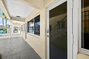 A covered outdoor corridor with a tiled floor, a sliding glass door, and a view of a pool and palm trees.