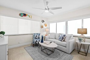 A living room with a white sofa, a round coffee table, a patterned armchair, and a ceiling fan.