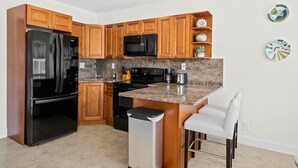 A modern kitchen with wooden cabinets, a black refrigerator, a microwave, and a granite countertop. - Bermuda Isles Villas - Queen #11 (Lauderdale-by-the-Sea)