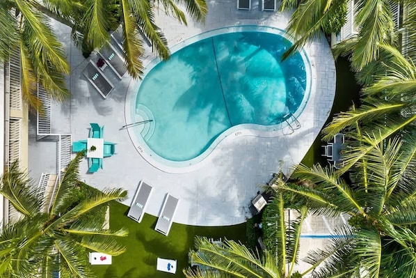 An aerial view of a swimming pool surrounded by palm trees, with lounge chairs and a small deck area.