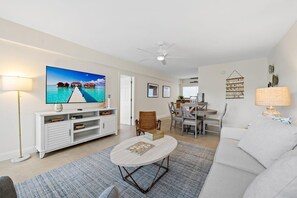 Un salon équipé d’un téléviseur, de meubles blancs, d’un coin repas et d’un ventilateur de plafond.