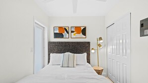 Une chambre à coucher avec un lit, deux tableaux abstraits accrochés au mur, une lampe de chevet et une porte.