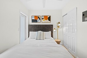 A bedroom with a bed, two wall-mounted abstract paintings, a bedside lamp, and a door.