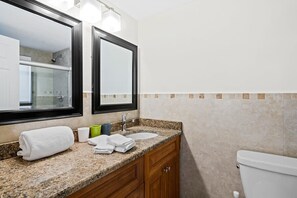 A bathroom with a granite countertop, a sink, a mirror, and a toilet.