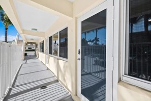 A covered outdoor corridor with a white railing, a tiled floor, and a view of a balcony with a metal railing. - Bermuda Isles Villas - Queen #14 (Lauderdale-by-the-Sea)