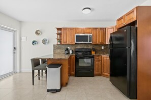 A modern kitchen with wooden cabinets, a black refrigerator, a microwave, an oven, and a coffee maker. - Bermuda Isles Villas - Queen #14 (Lauderdale-by-the-Sea)