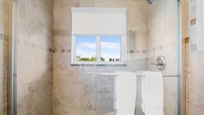 Eine bodenebene Dusche mit Glastür, ein Fenster und zwei Handtücher, die an einem Halter hängen.
