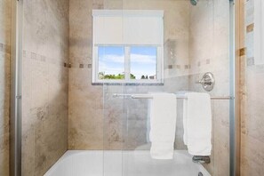 Eine bodenebene Dusche mit Glastür, ein Fenster und zwei Handtücher, die an einem Halter hängen.