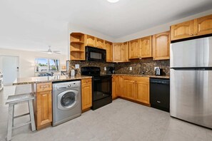 Una cocina moderna con armarios de madera, un refrigerador de acero inoxidable, un microondas, un lavavajillas y una lavadora.