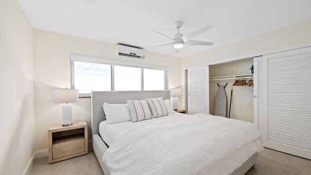 Une chambre à coucher comprenant un lit, des tables de chevet, un ventilateur de plafond, un appareil de climatisation, une fenêtre et une armoire.