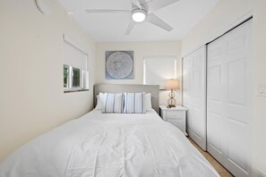 Un dormitorio con una cama, una mesita de noche, una lámpara, un ventilador de techo y un armario.