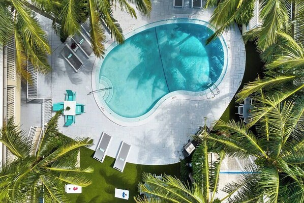 Vista aérea de una piscina rodeada de palmeras y un patio con sillas de descanso y una mesa.