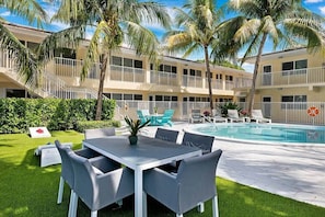 Un patio de hotel con piscina, mobiliario exterior y palmeras.