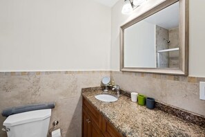 A bathroom with a toilet, sink, mirror, and shower area.