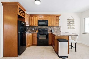 Cucina con mobili in legno, frigorifero nero, microonde, piano cottura e cestino.