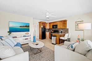 A modern living room with a flat-screen TV, a dining area, and a kitchen with wooden cabinets.