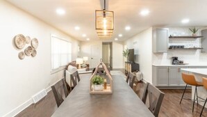 A modern kitchen with white cabinets, a wooden dining table, and a pendant light.