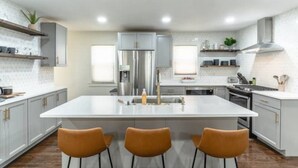 A modern kitchen with a central island, white cabinetry, and three brown bar stools.