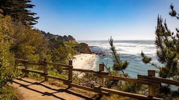 A coastal path with a wooden fence, leading to a beach with ocean views.