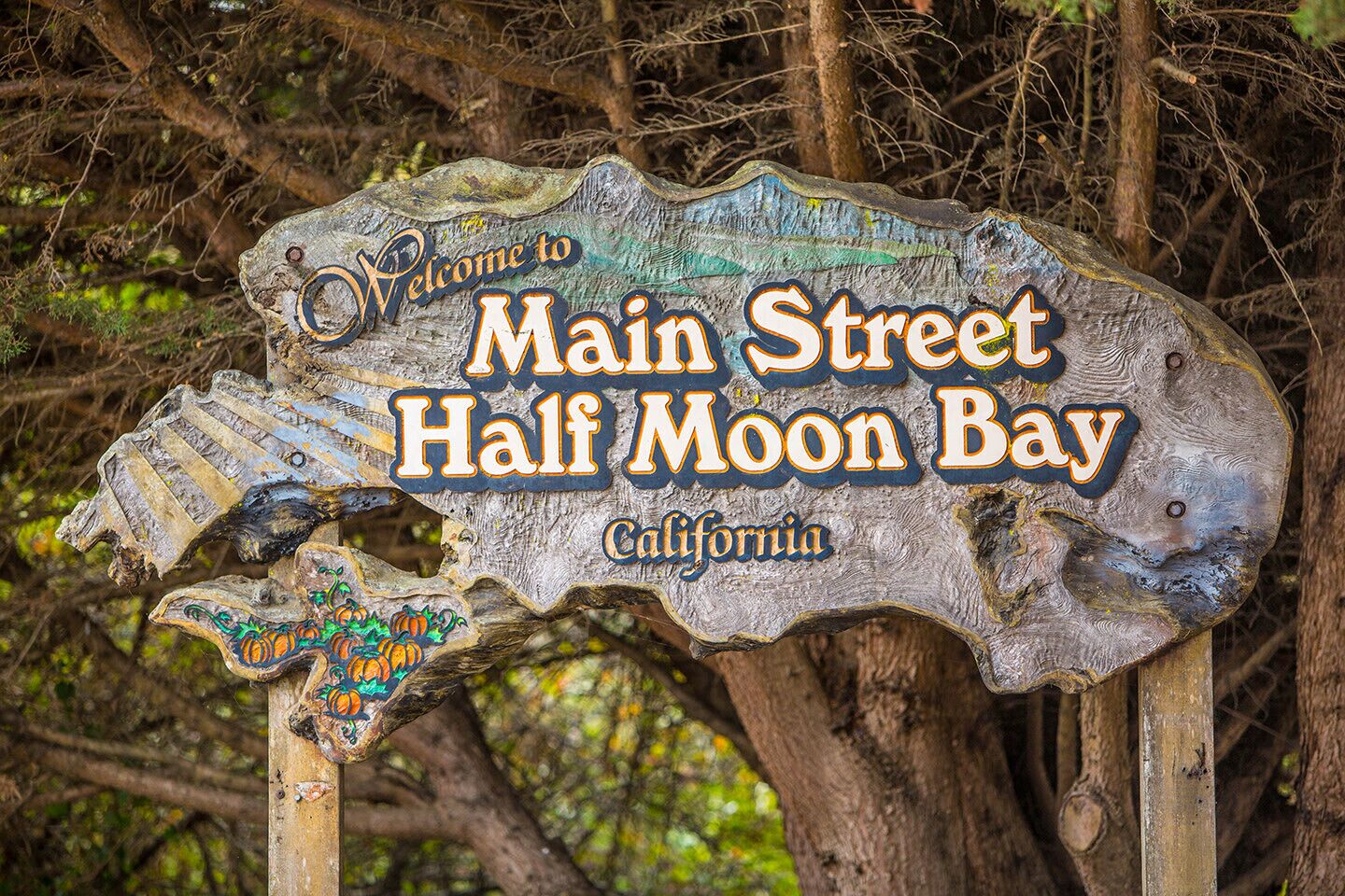 A rustic wooden sign with the text "Welcome to Main Street Half Moon Bay, California."