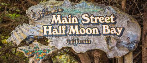 A rustic wooden sign with the text "Welcome to Main Street Half Moon Bay, California."