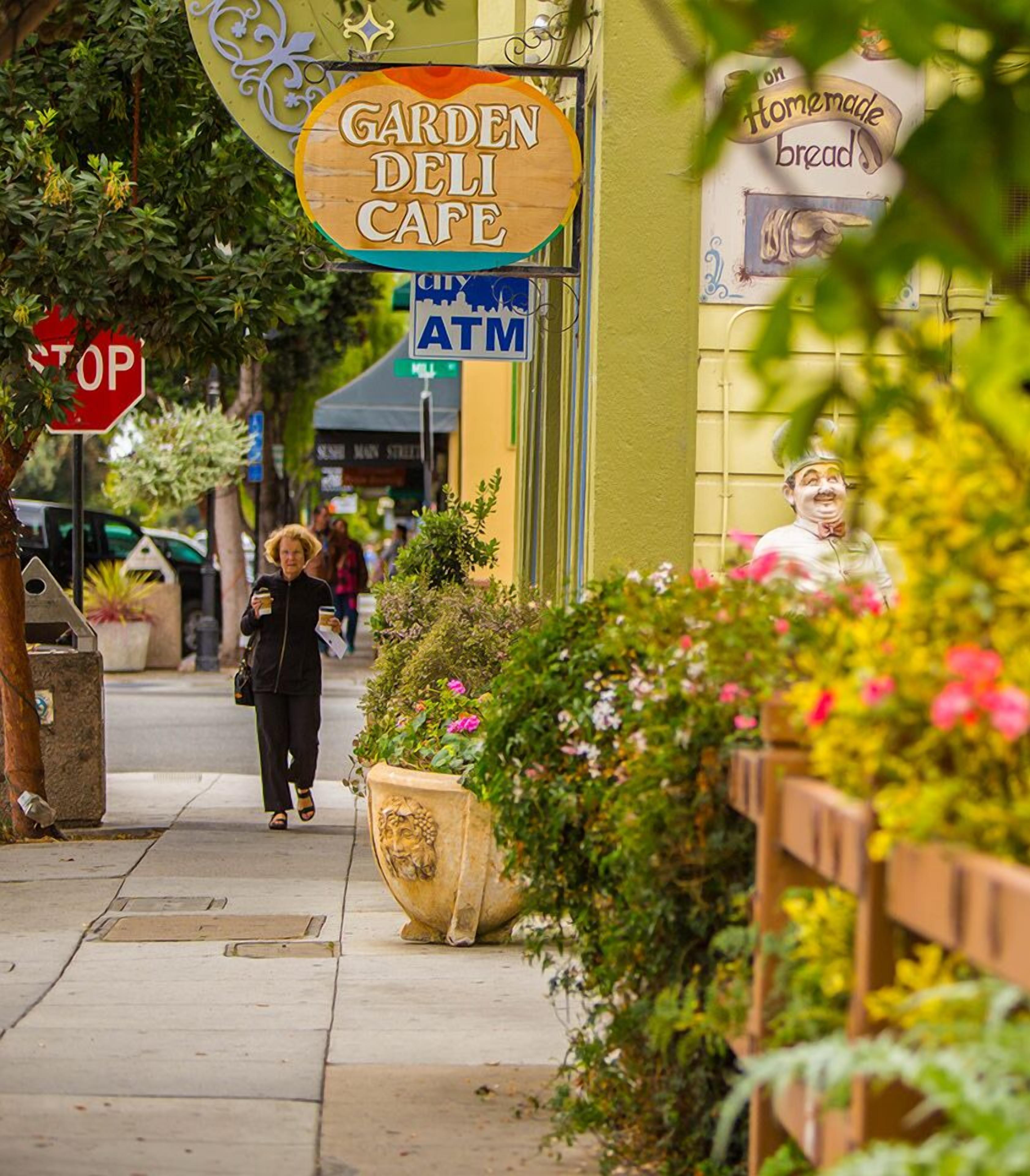 A street with a 'Garden Deli Cafe' sign, an ATM, and a 'Stop' sign.