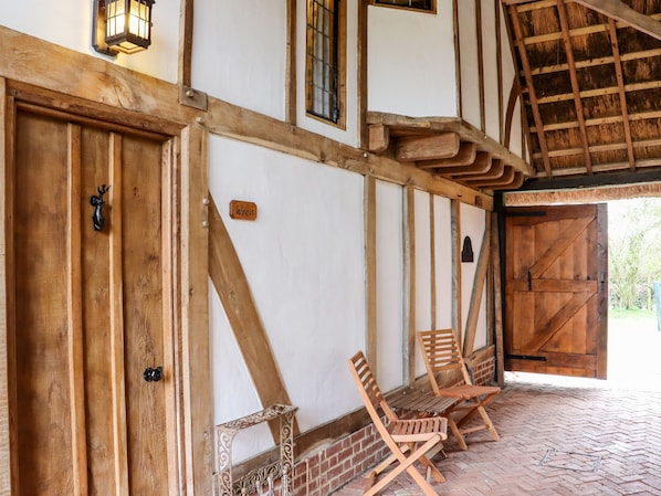 A rustic wooden building with a thatched roof, a large wooden door, and two wooden chairs outside.