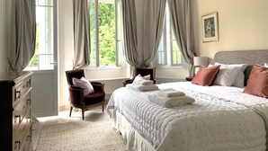 A bedroom with a large bed, two chairs, a dresser, and a chandelier.