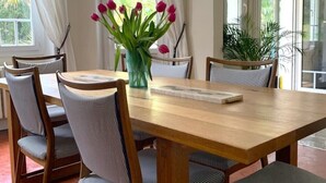 A dining area with a wooden table and chairs, a vase with flowers, and large windows with curtains.