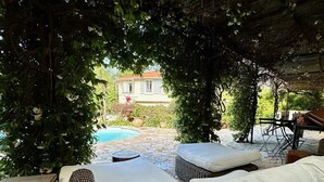 An outdoor seating area with wicker furniture, a stone pool, and a view of a house in the background.