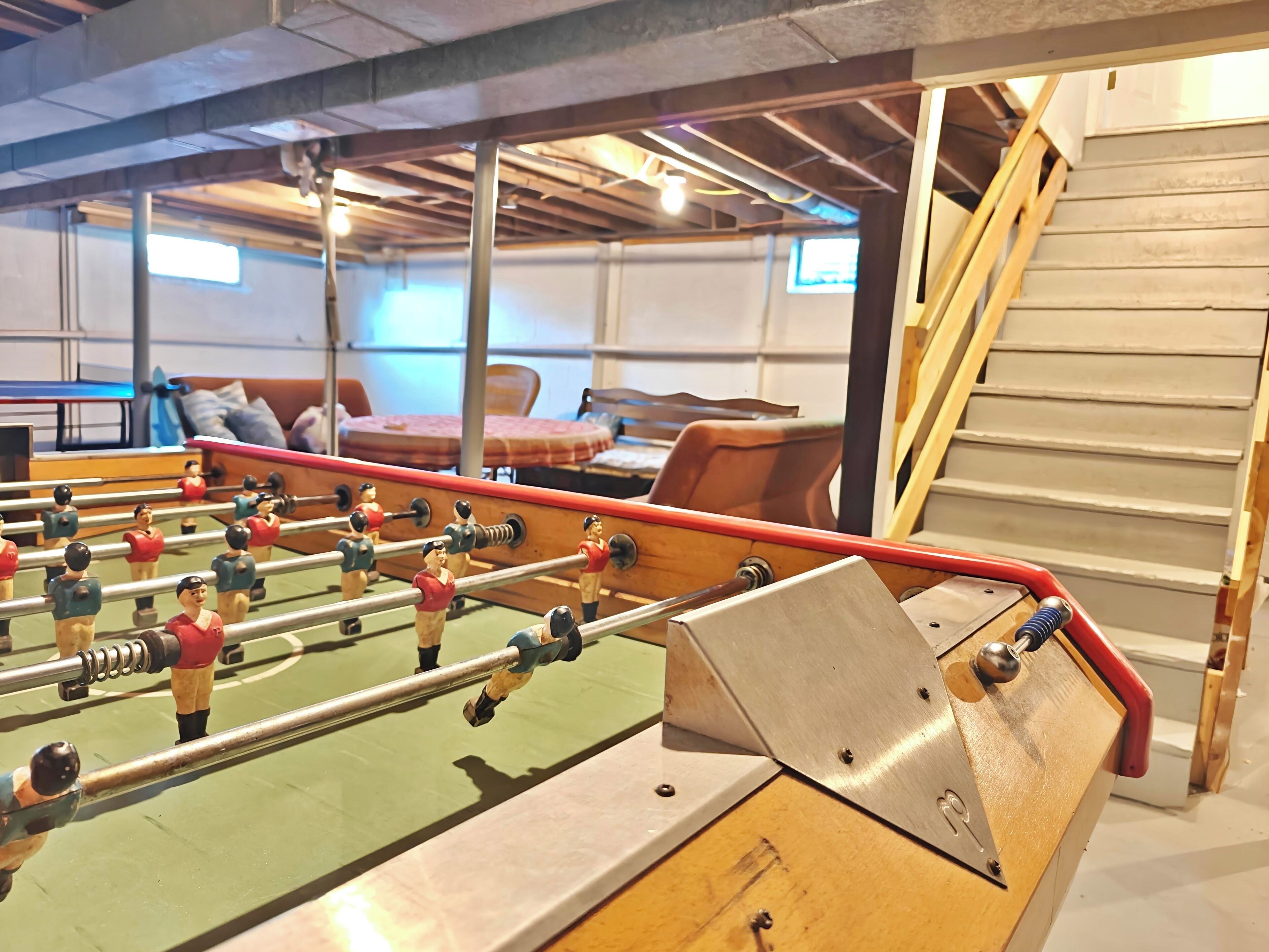 A foosball table in a room with a staircase and a bed in the background.