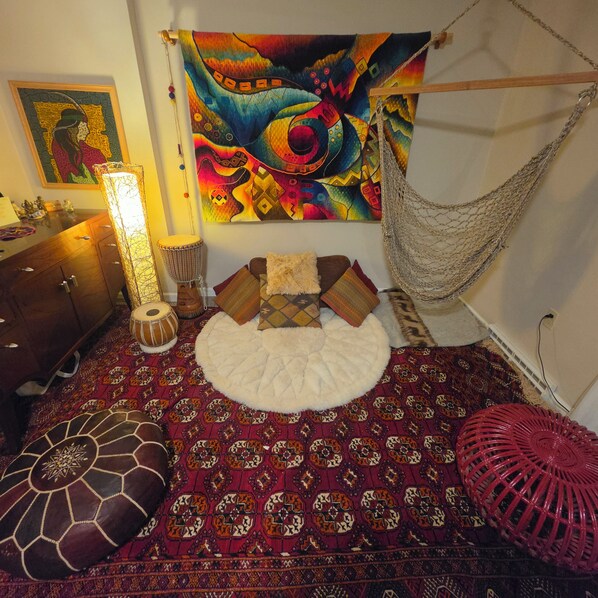 A room with a patterned carpet, a hammock, a drum, and a tapestry on the wall.