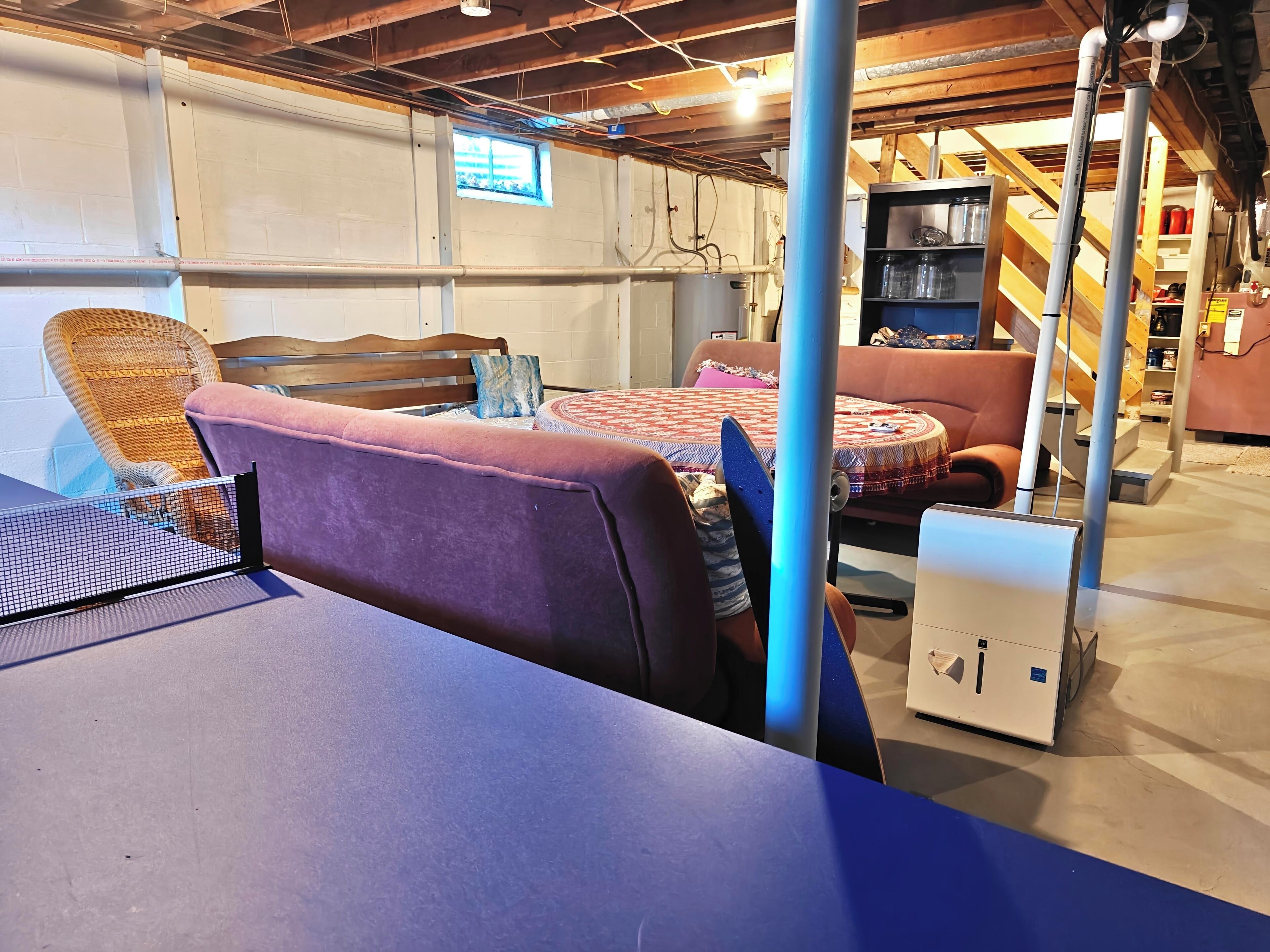 Une pièce avec un lit, une chaise et une table. On aperçoit des tuyaux et une échelle au fond.